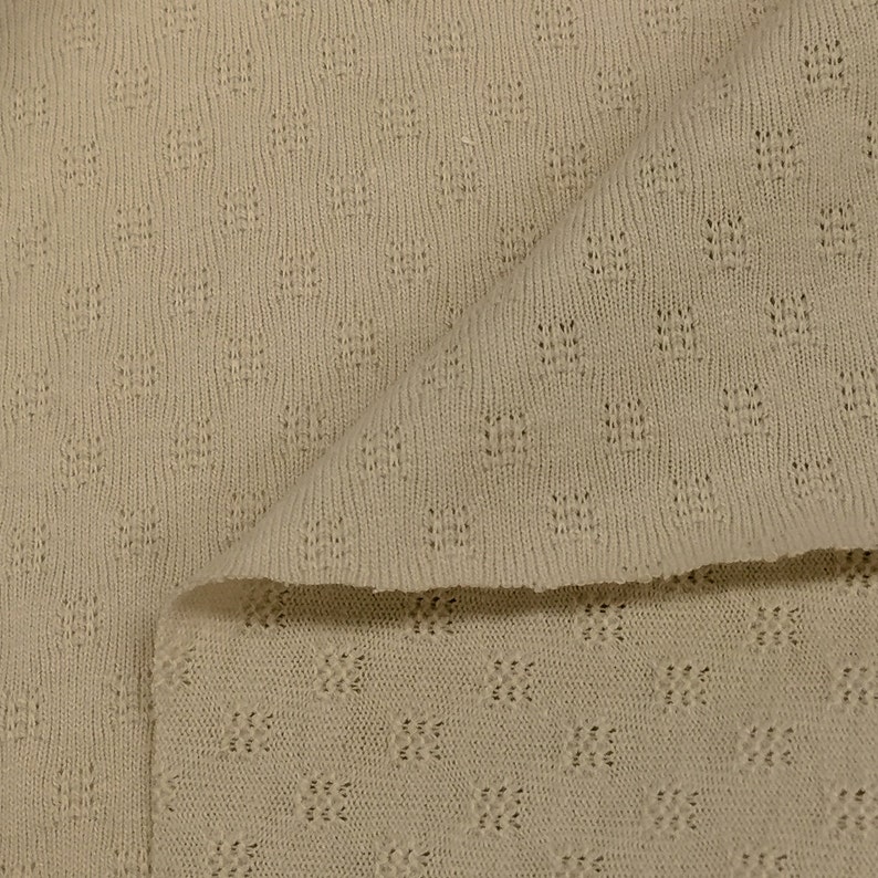 May include: A close-up of a beige knitted fabric with a textured pattern. The fabric is folded in half, showing the pattern on both sides.