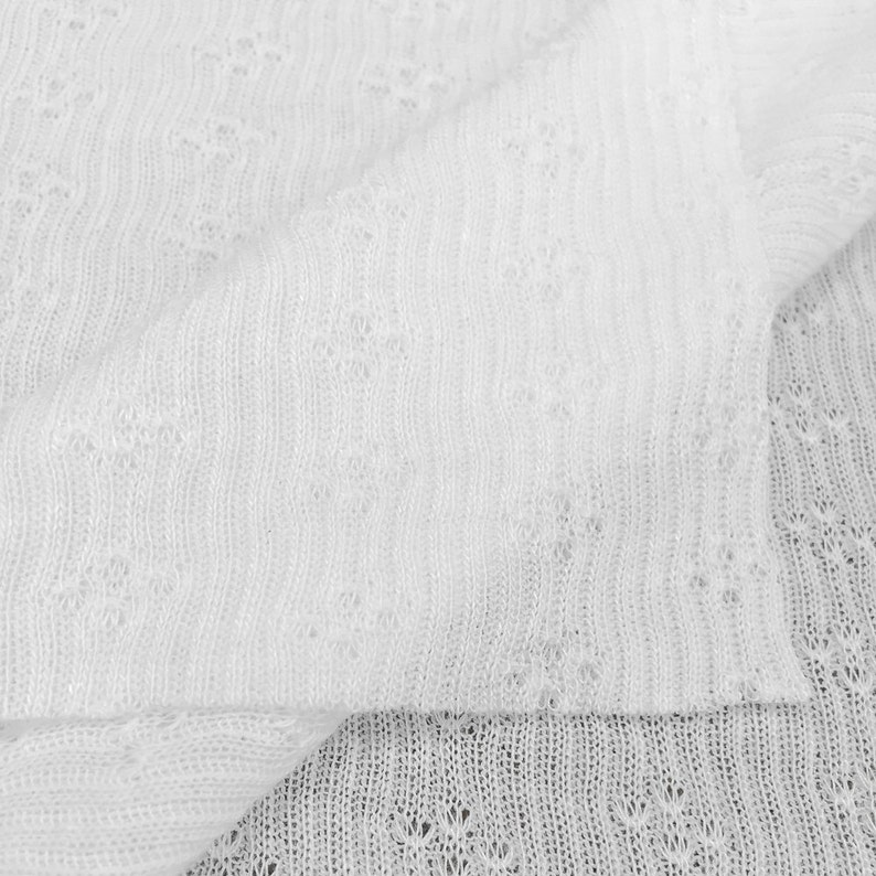 May include: White knitted fabric with a delicate openwork pattern. The fabric is soft and lightweight, making it ideal for a variety of projects.