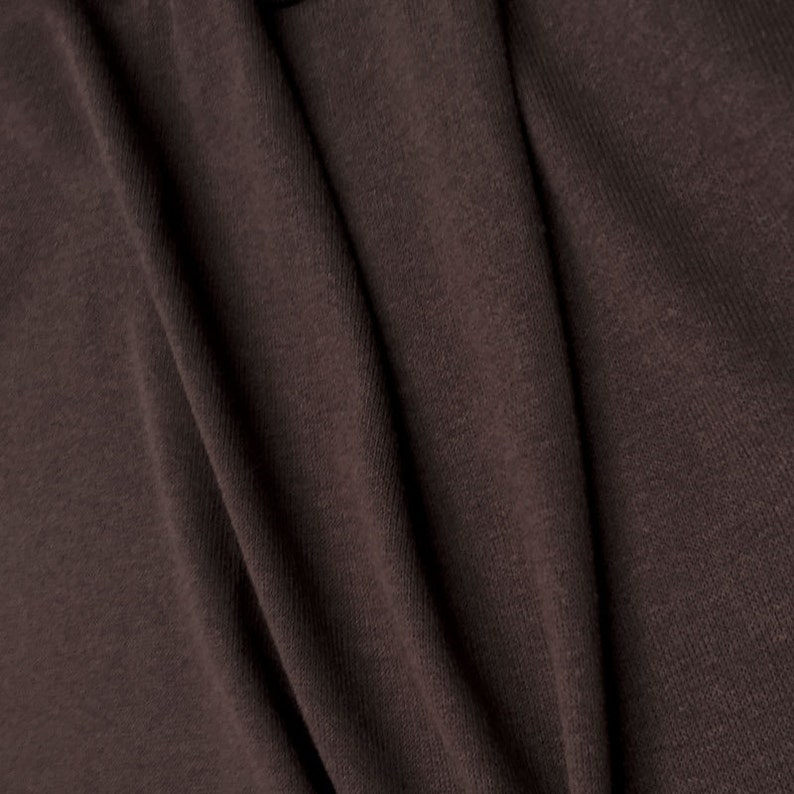 May include: Close-up of a brown fabric with a textured surface. The fabric is folded and has a soft, smooth feel.