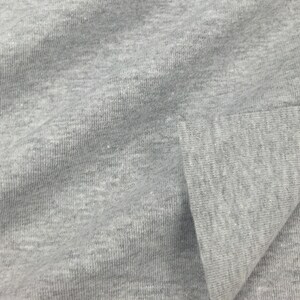 May include: Close-up of a gray, textured fabric with a subtle ribbed pattern. The fabric is folded over, showing the inside of the material.