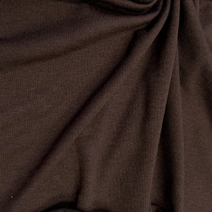 May include: Close-up of a brown fabric with a textured surface. The fabric is folded and draped, showing its soft and smooth texture.