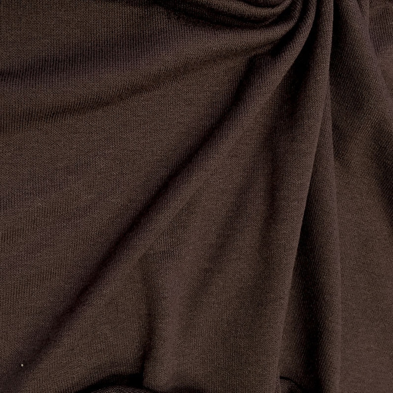 May include: Close-up of a brown fabric with a textured surface. The fabric is folded and draped, showing its soft and smooth texture.