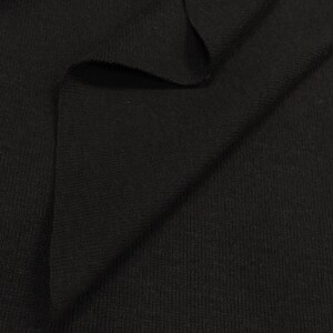 May include: Black ribbed knit fabric. The fabric is folded in half, showing the texture of the knit.
