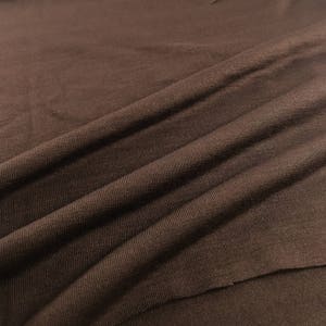 May include: Close-up of a brown fabric with a smooth, textured surface. The fabric is folded and draped, showing its soft and pliable nature.