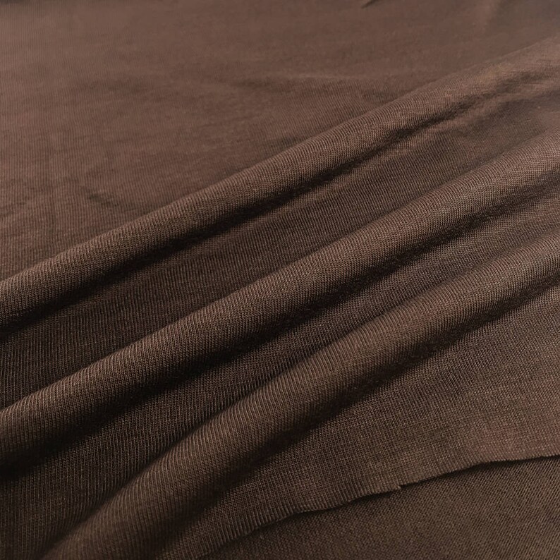 May include: Close-up of a brown fabric with a smooth, textured surface. The fabric is folded and draped, showing its soft and pliable nature.