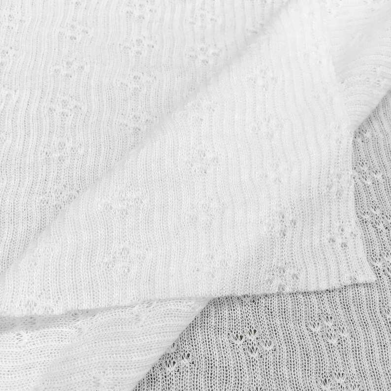 May include: White knitted fabric with a delicate openwork pattern. The fabric is soft and lightweight, making it ideal for clothing or home decor.