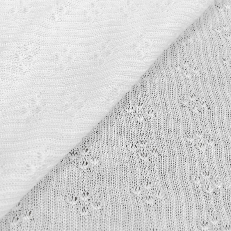 May include: Close-up of two sections of white, open-weave fabric. The fabric has a delicate, lacy appearance with small, repeating floral patterns. The texture is soft and airy, suggesting a lightweight material suitable for clothing or decorative items.