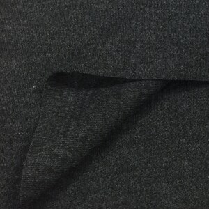 Puede incluir: Primer plano de una tela de punto de canal&eacute; gris oscuro. La tela est&aacute; doblada sobre s&iacute; misma, mostrando la textura del material.