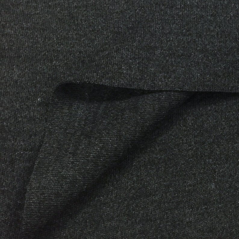 Puede incluir: Primer plano de una tela de punto de canal&eacute; gris oscuro. La tela est&aacute; doblada sobre s&iacute; misma, mostrando la textura del material.
