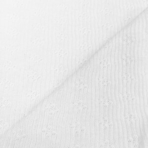 May include: White fabric with a delicate, openwork floral pattern. The fabric is folded, showing the texture and the interplay of light and shadow. The material appears to be soft and lightweight, suitable for various sewing projects.
