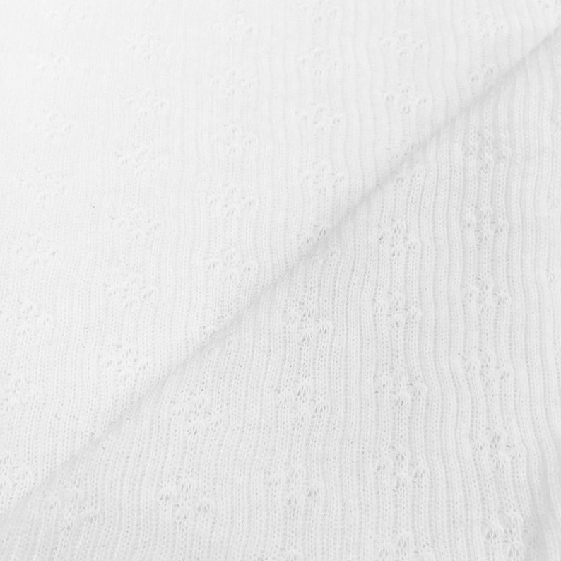 May include: White fabric with a delicate, openwork floral pattern. The fabric is folded, showing the texture and the interplay of light and shadow. The material appears to be soft and lightweight, suitable for various sewing projects.