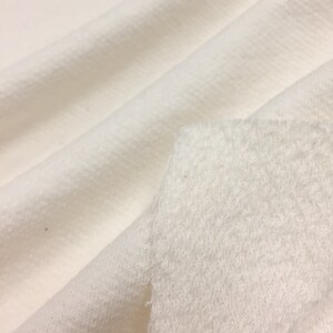May include: Close-up of a white fabric with a textured surface. The fabric is soft and fluffy, and it appears to be a type of fleece.