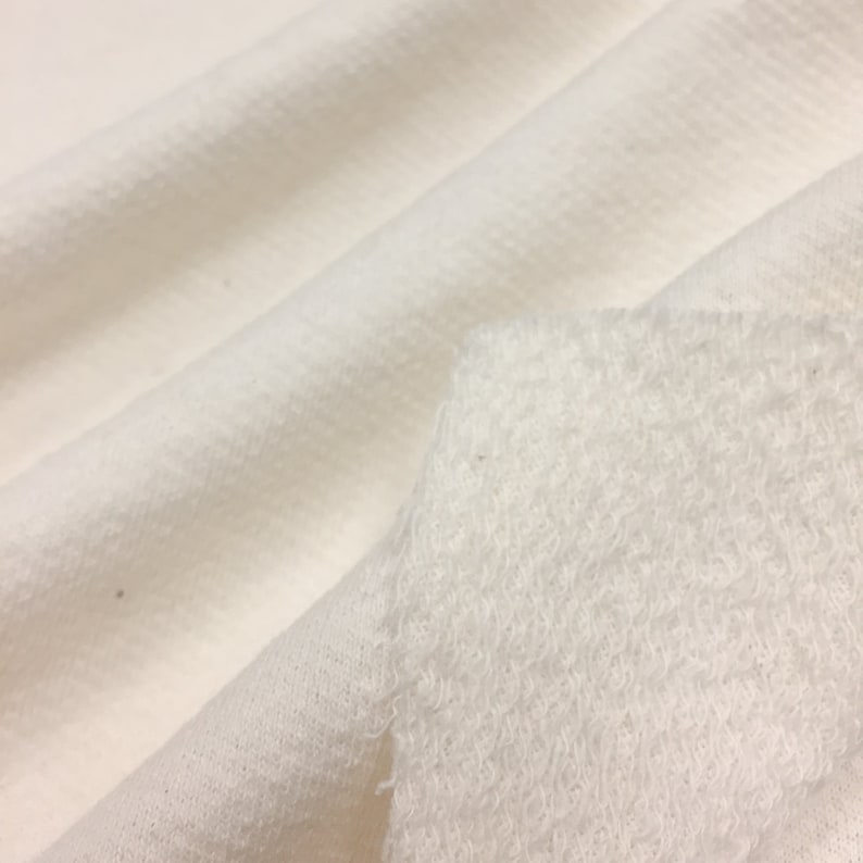 May include: Close-up of a white fabric with a textured surface. The fabric is soft and fluffy, and it appears to be a type of fleece.