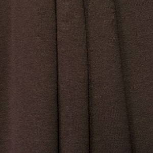 May include: Close-up of a dark brown fabric with a textured, woven appearance. The fabric is folded in several places, creating a series of vertical lines.