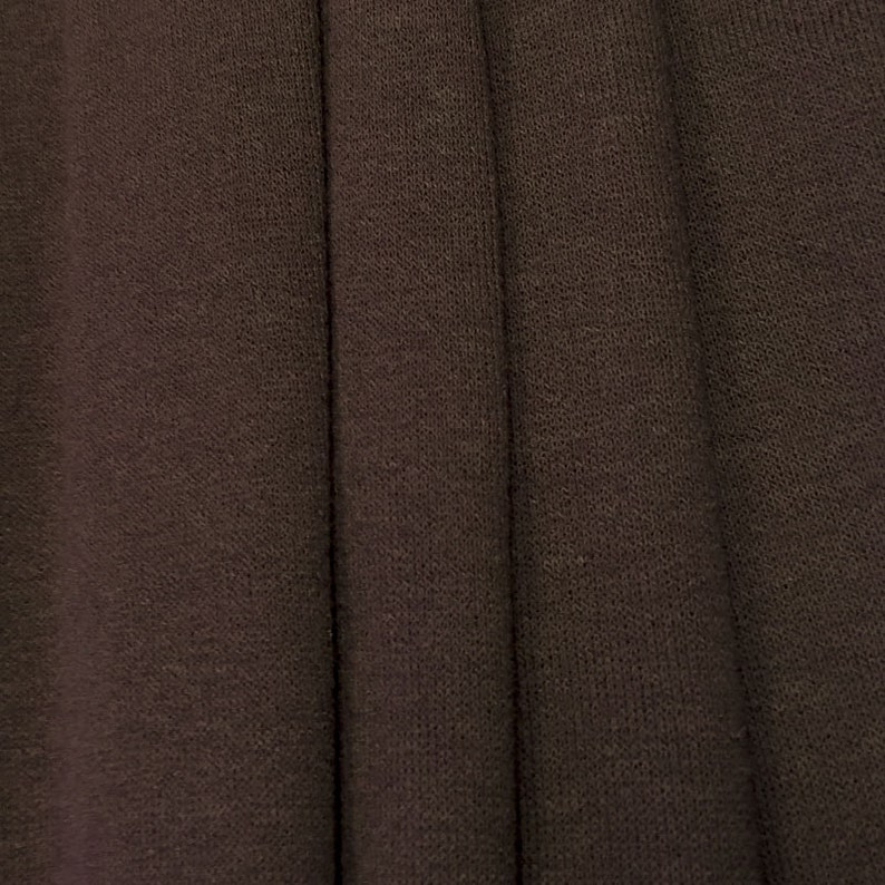 May include: Close-up of a dark brown fabric with a textured, woven appearance. The fabric is folded in several places, creating a series of vertical lines.