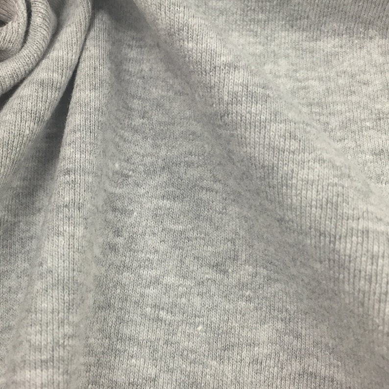 May include: Close-up of a gray, textured fabric with a subtle ribbed pattern. The fabric is soft and has a slightly fuzzy texture.