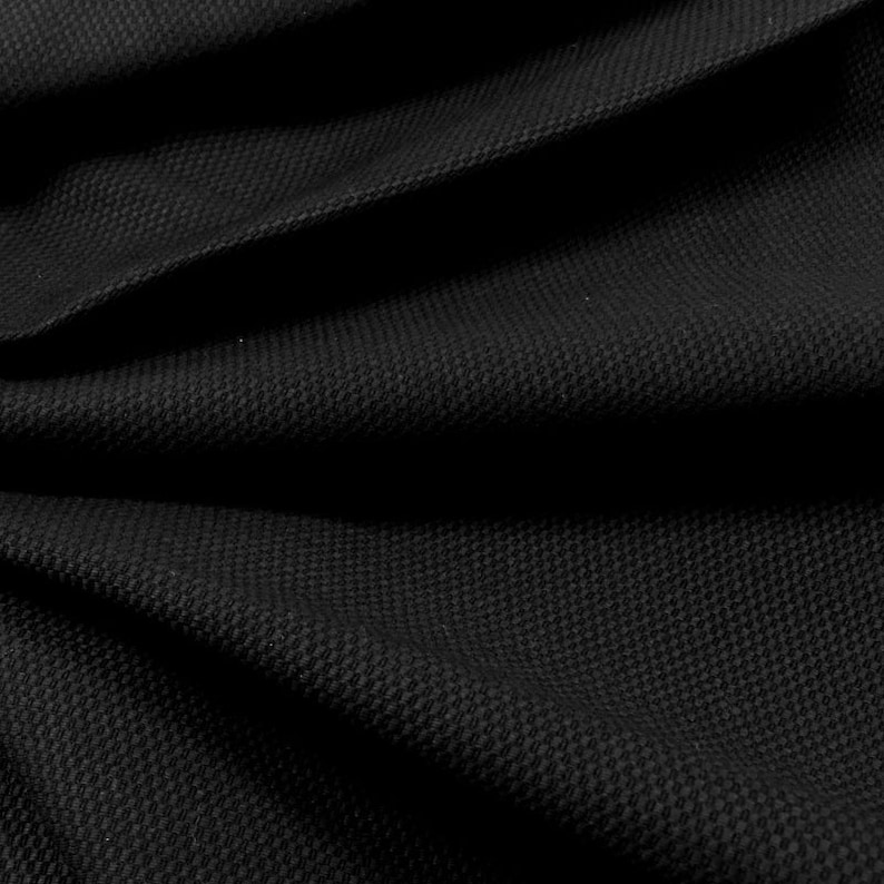 May include: Black fabric with a textured weave. The fabric is folded and draped, showing the texture and drape of the material.
