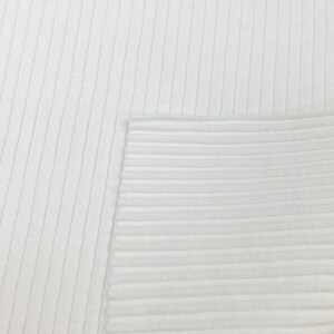 Op de afbeelding: Witte ribbelstof met een gladde textuur. De stof is geweven met verticale lijnen.