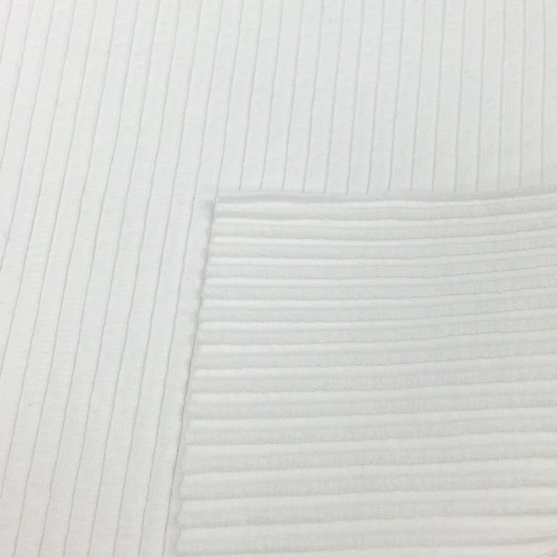 Op de afbeelding: Witte ribbelstof met een gladde textuur. De stof is geweven met verticale lijnen.