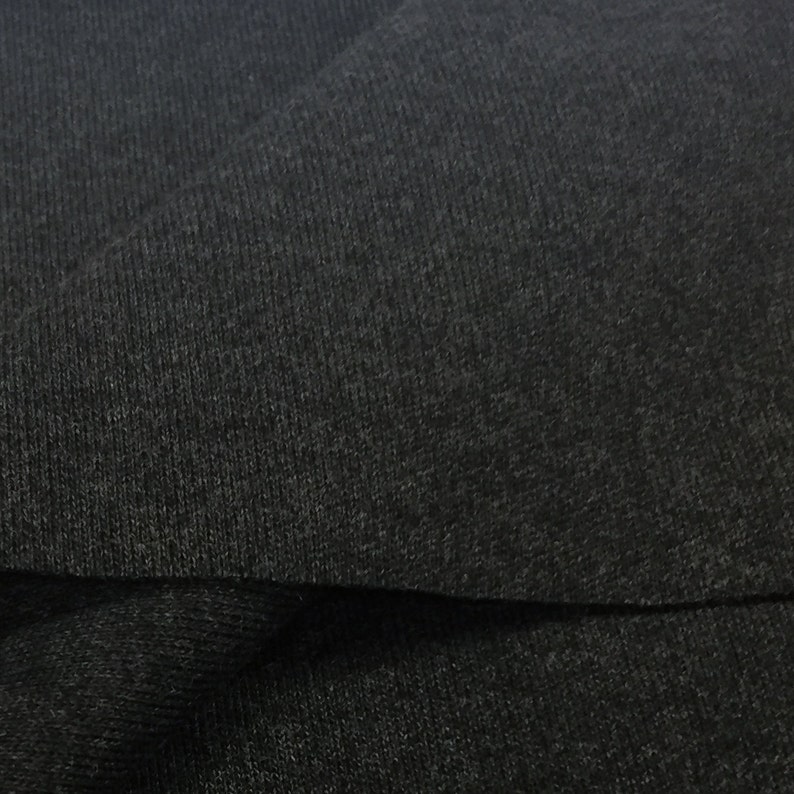 Puede incluir: Primer plano de una tela gris oscuro con una superficie texturizada y acanalada. La tela est&aacute; doblada, mostrando el interior del material.