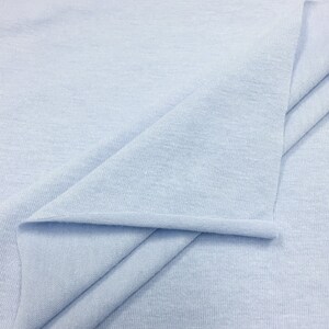 May include: A close-up of a light blue fabric with a smooth, even texture. The fabric is folded in a way that shows the soft, drapey quality.