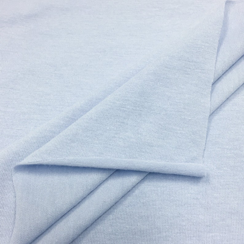 May include: A close-up of a light blue fabric with a smooth, even texture. The fabric is folded in a way that shows the soft, drapey quality.