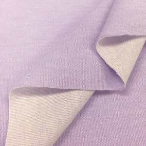 May include: A close-up of a soft, lilac-colored fabric with a white underside. The fabric is folded in half, showing both sides.