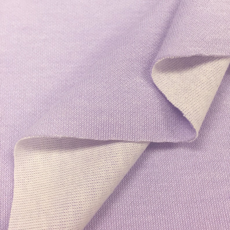 May include: A close-up of a soft, lilac-colored fabric with a white underside. The fabric is folded in half, showing both sides.