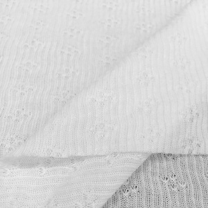 May include: Close-up of white fabric with a delicate, open weave. The material is folded, showing the texture and pattern of the knit. The fabric appears soft and lightweight, suitable for clothing or accessories.