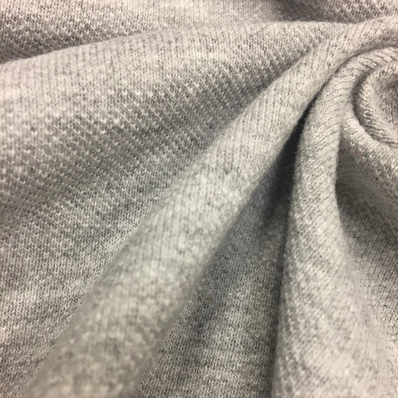 Puede incluir: Primer plano de una tela gris texturizada con un aspecto suave y peludo. La tela est&aacute; doblada y drapeada, mostrando su textura y ca&iacute;da.