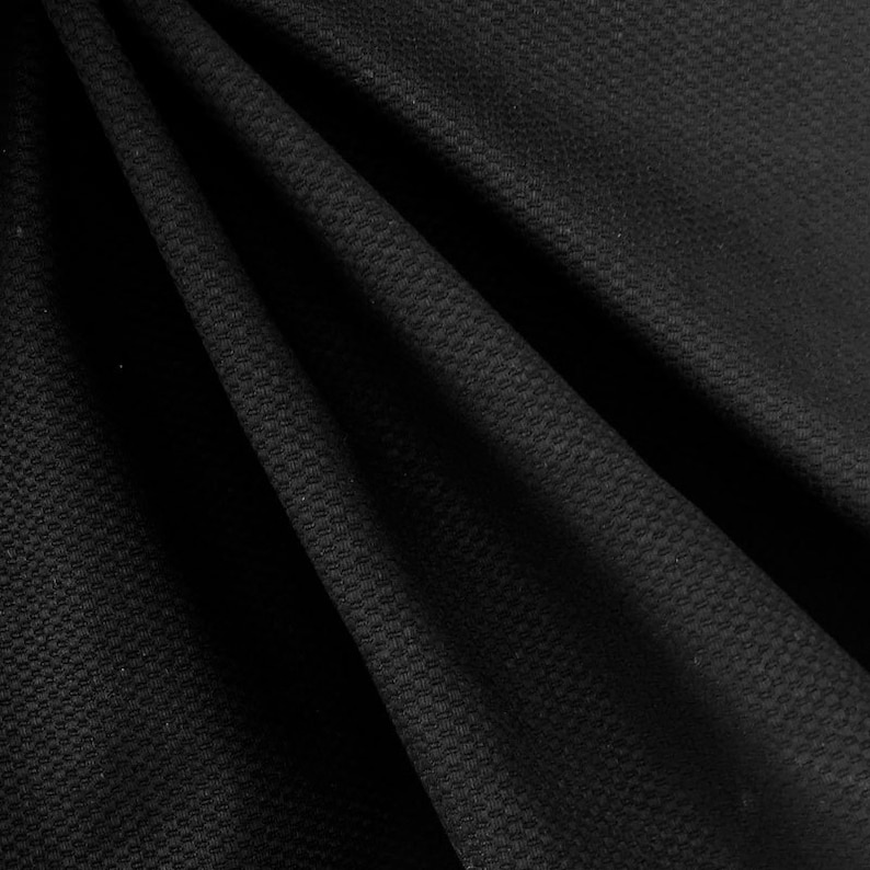 May include: Black textured fabric with a subtle waffle weave pattern. The fabric is folded and draped, showcasing its texture and drape.