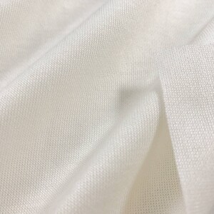 May include: Close-up of a white, soft, and textured fabric. The fabric is folded and has a smooth, even surface.