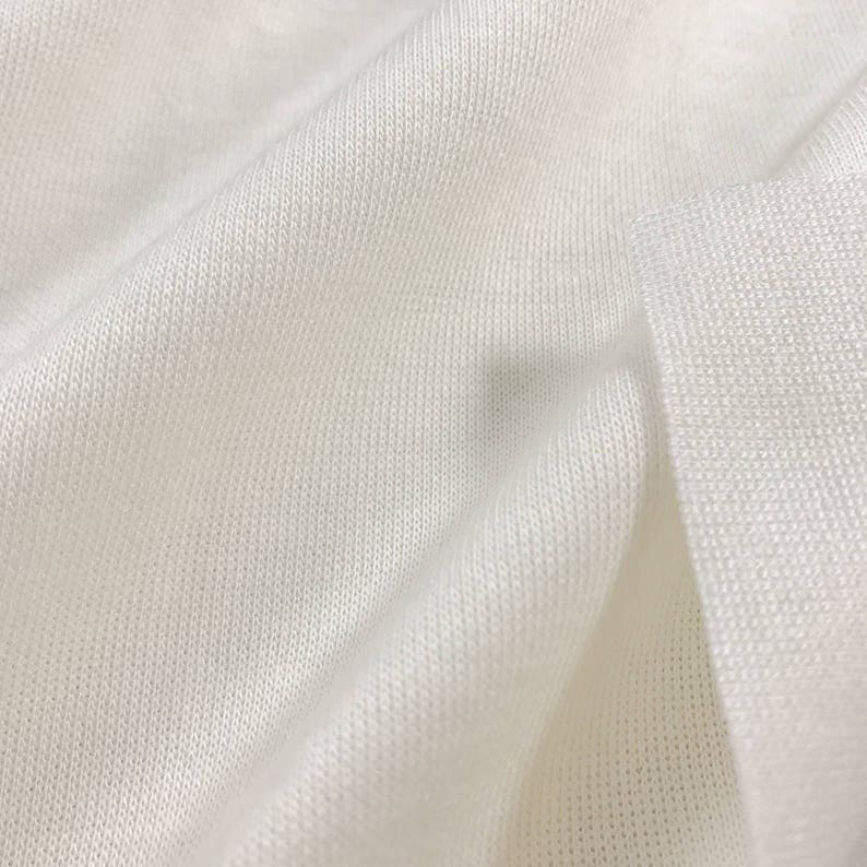May include: Close-up of a white, soft, and textured fabric. The fabric is folded and has a smooth, even surface.