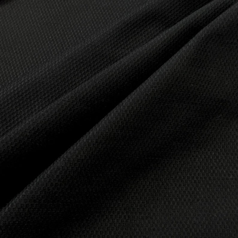 May include: Black textured fabric with a subtle waffle weave pattern. The fabric is folded in a diagonal fold, creating a soft, draping effect.