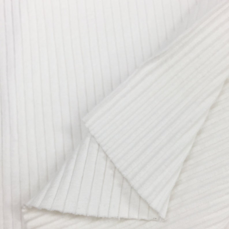 Op de afbeelding: Witte ribbelstof met een gladde textuur. De stof is dubbelgevouwen, waardoor het ribbelpatroon aan beide kanten zichtbaar is.