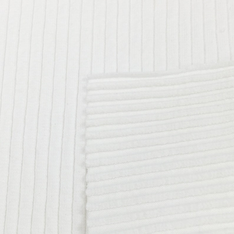 Op de afbeelding: Close-up van witte ribbelstof. De stof heeft een gladde textuur en een subtiele glans.