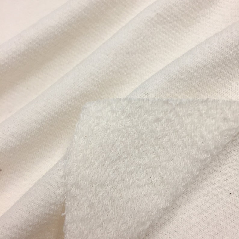 May include: Close-up of a white fabric with a soft, fuzzy texture on one side and a smooth, woven texture on the other side.