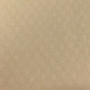 May include: A close-up of a beige knitted fabric with a textured pattern.