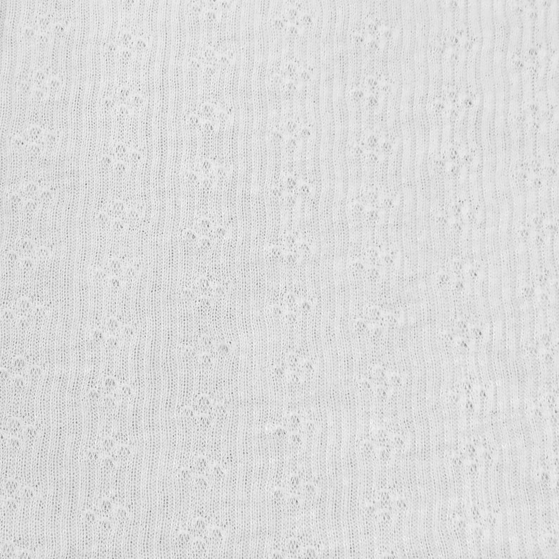 May include: White knitted fabric with a textured pattern. The fabric has a soft, delicate look and feel.