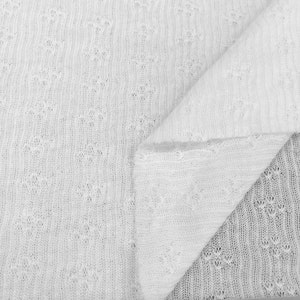 May include: White knitted fabric with a delicate openwork pattern. The fabric is folded in half, showing the texture and detail of the knit.