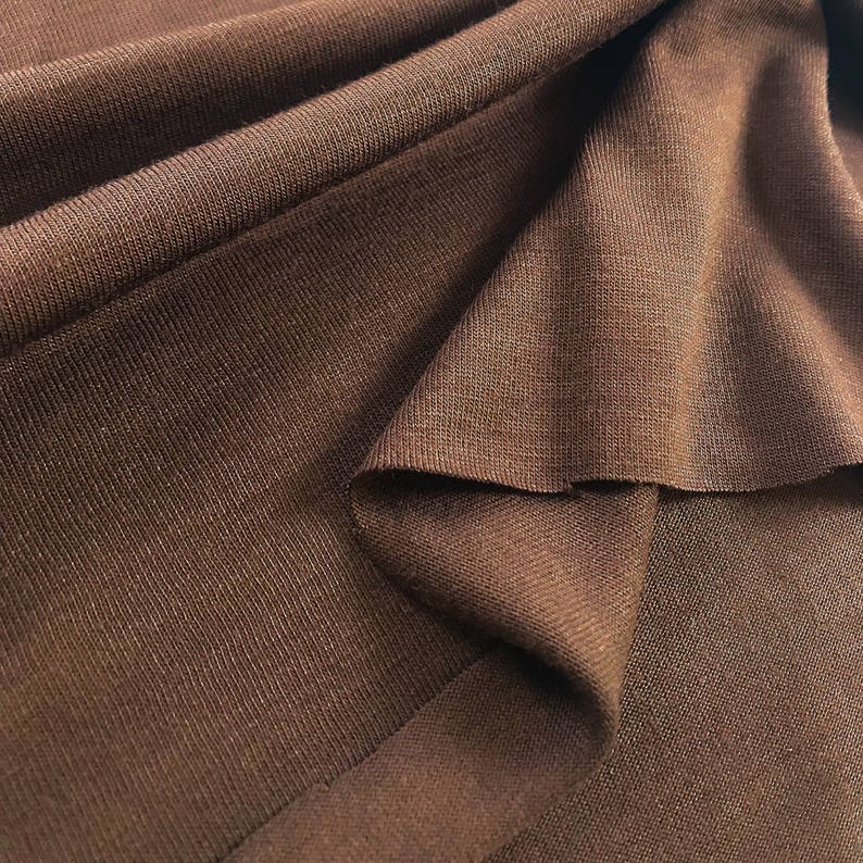 May include: Close-up of a brown fabric with a textured surface. The fabric is folded and draped, showing its soft and smooth texture.