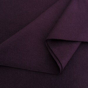 Puede incluir: Primer plano de una tela de color morado oscuro con un patr&oacute;n de punto texturizado. La tela est&aacute; doblada sobre s&iacute; misma, mostrando el interior del material.