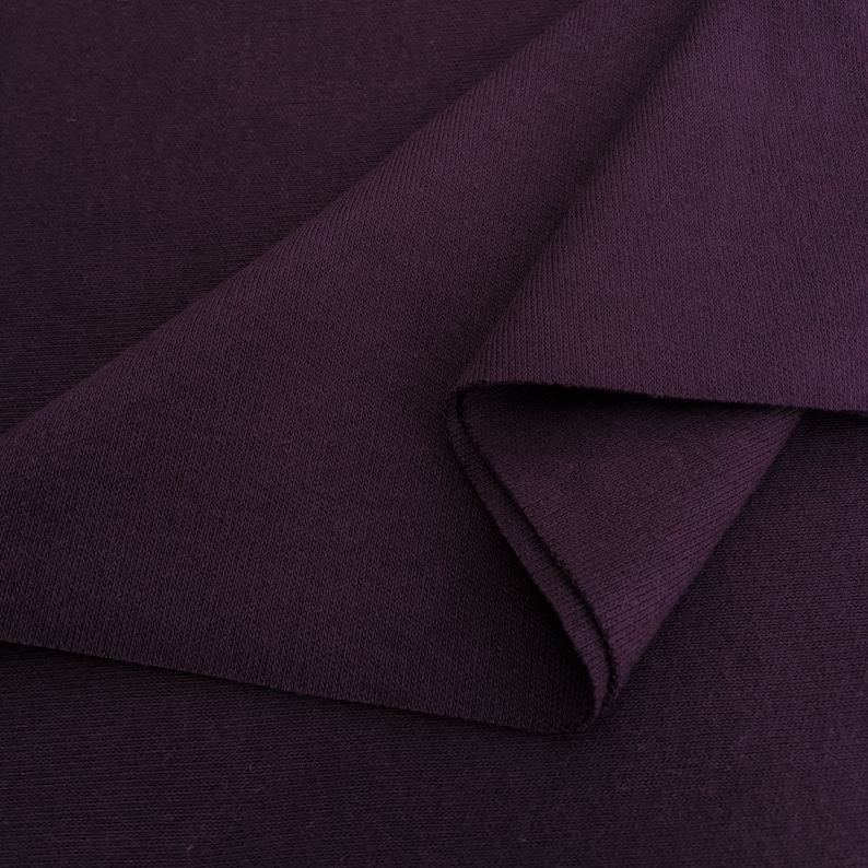 Puede incluir: Primer plano de una tela de color morado oscuro con un patr&oacute;n de punto texturizado. La tela est&aacute; doblada sobre s&iacute; misma, mostrando el interior del material.