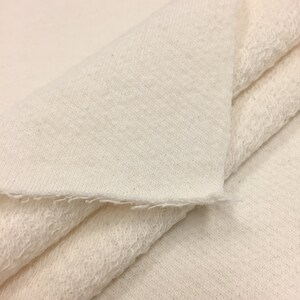 May include: Close-up of a white, soft, and textured fabric. The fabric is folded in half, showing the inside and outside of the material.