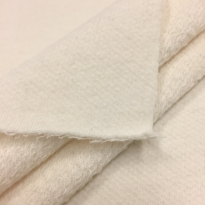 May include: Close-up of a white, soft, and textured fabric. The fabric is folded in half, showing the inside and outside of the material.