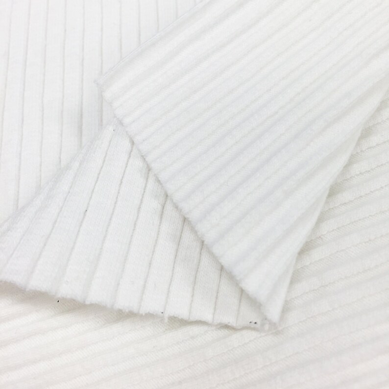 Op de afbeelding: Witte ribbelstof met een textuur. De stof is dubbelgevouwen, waardoor de binnen- en buitenkant van het materiaal zichtbaar is.