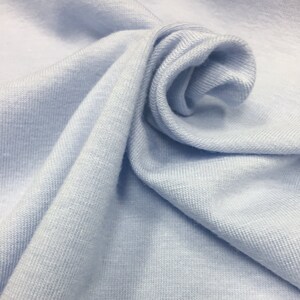 May include: A close-up of a light blue fabric with a soft, textured surface. The fabric is folded and draped, creating a smooth, flowing look.