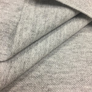 Puede incluir: Primer plano de una tela gris texturizada. La tela est&aacute; doblada en varios lugares, mostrando la textura suave y de punto.