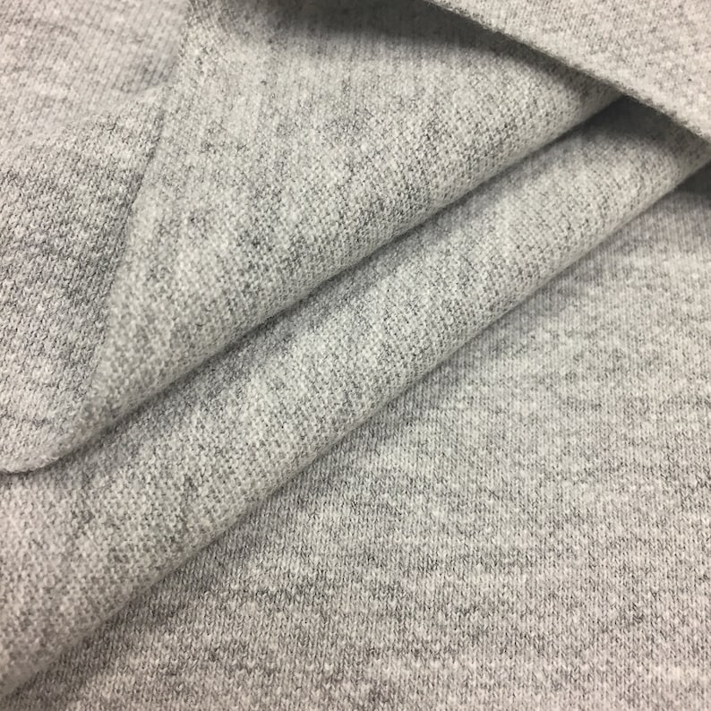 Puede incluir: Primer plano de una tela gris texturizada. La tela est&aacute; doblada en varios lugares, mostrando la textura suave y de punto.