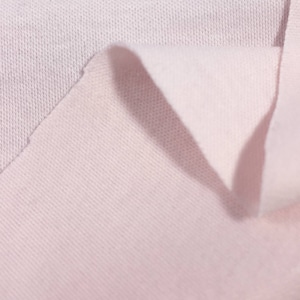 May include: Close-up of a soft, pale pink fabric with a textured surface. The fabric is folded over, revealing the underside.